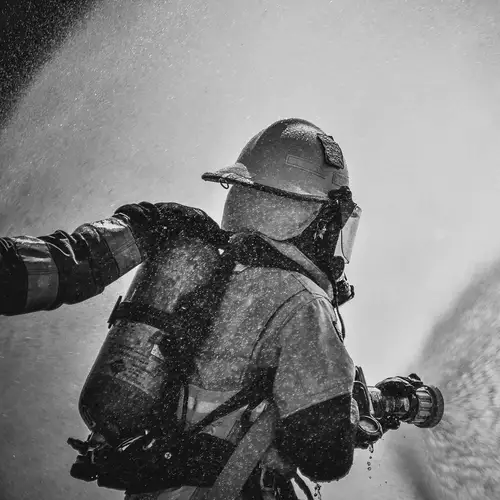 A firefighter shooting his hose, while another firefighter is holding his shoulder