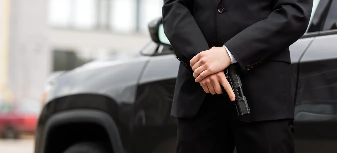 A body guard in a nice suit stands guard at a vehicle with a pistol