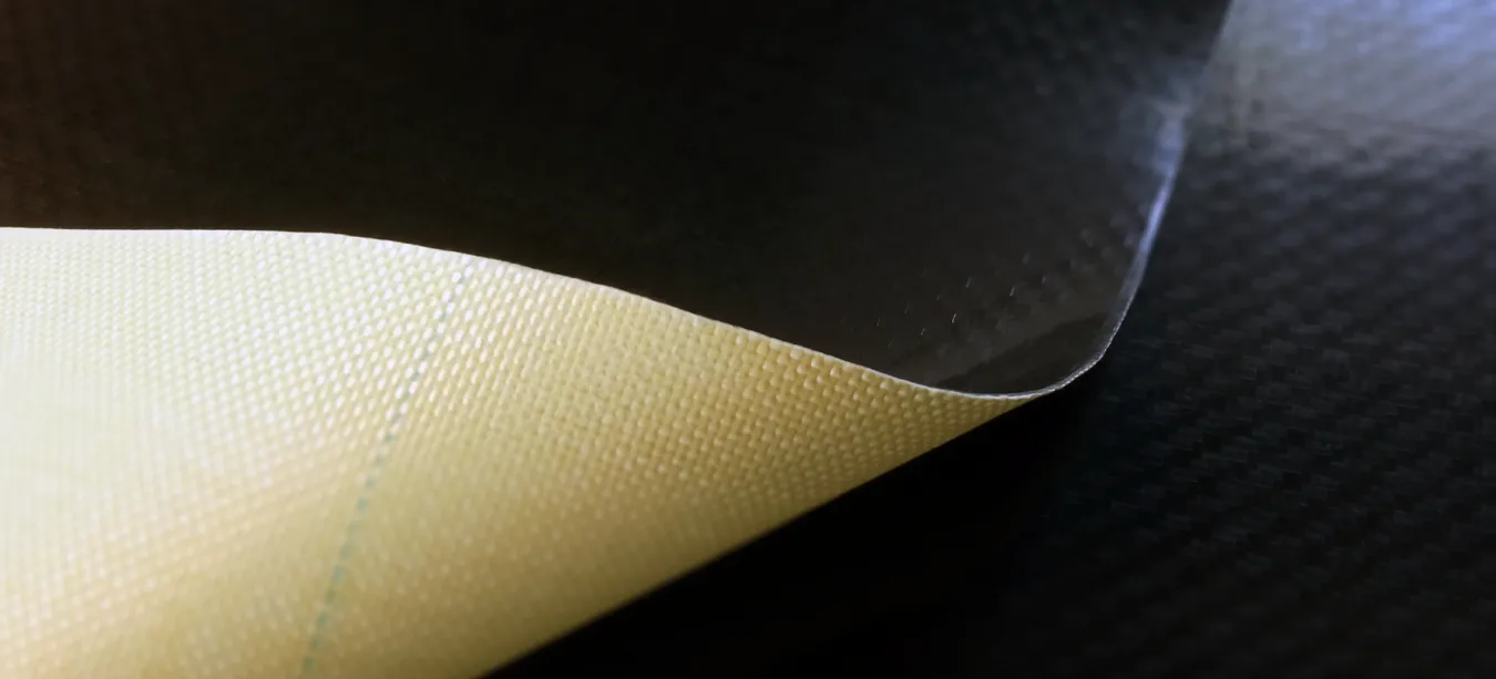 A curling roll of material, showing the bond between a yellow aramid layer and a carbon fiber topside